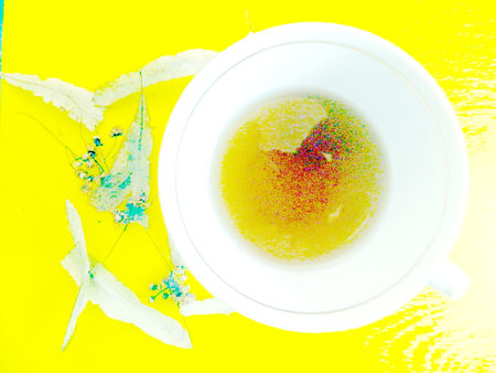 A small incomplete cup with tea from lime flowers and scattered dried linden flowers and leaves near the cup on the blackboardの写真素材