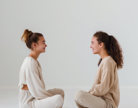Portrait of two young women sitting back to back and looking at each otherの素材