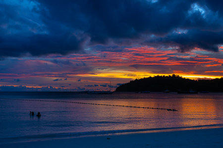 The calm evening sea contrasts with the colorful sky behind the sunset.の写真素材