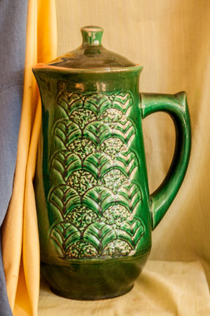 Green vase with floral ornament in the center against the background of draperies, yellow and blueの写真素材
