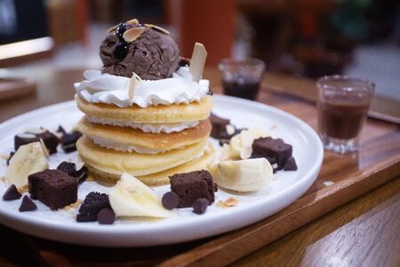 Pancakes with bananas and brownies topped with whipped cream and chocolate ice creamの写真素材