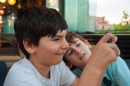 Two boy enjoy playing online games. One boy is watching. Young boys use their phones for learning in a bar or at homeの写真素材