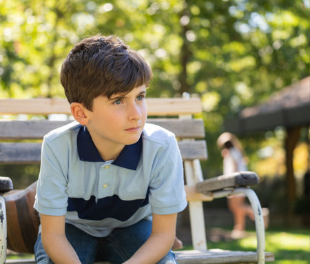 portrait of handsome caucasian teenage child boy sitting on bench in a park looking away. Beautiful sunny dayの写真素材