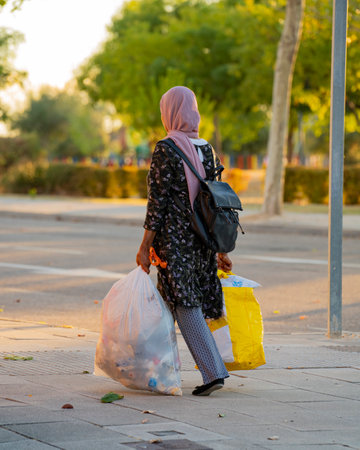 Islamic woman walking with rubbish. Rear view of a muslim or Arab young girl carrying garbage bagsの写真素材