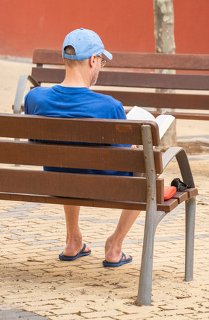 Adult man with a blue cap relaxed reading on park benchの写真素材