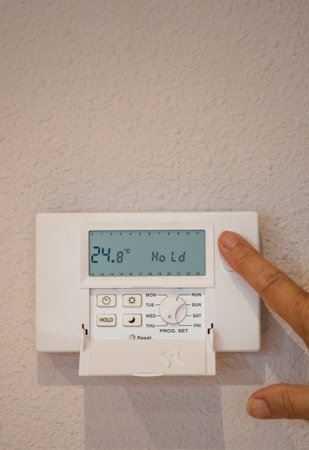 Close-up Of person hand setting Temperature On Digital Thermostat at home attached To Wall. Copy...