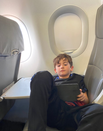 Cute boy having some rest lying down in passenger seat on airplane while watching the touch padの写真素材