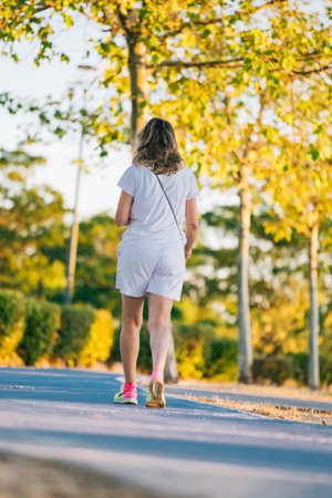 Rear view of a woman walking alone and calm through a park at sunset. Golden hour shadows and sun lightの写真素材