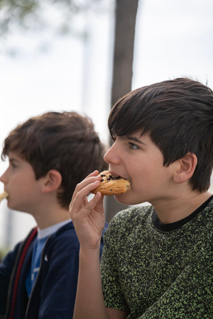 Close up portrait of boys sitting on a bench in park and eating a chocolate biscuit. side viewの写真素材