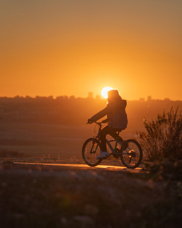Silhouette of woman riding a bicycle against the sun and Madrid cityscape at sunsetの写真素材