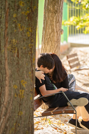 Mother and son enjoying time together on bench, hugging smiling with sun flare, outdoors. Happy expressions, family fun.の写真素材