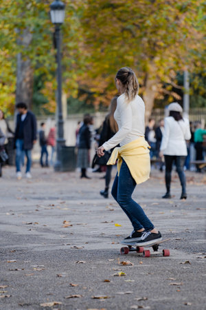 Rear view of young sporty woman riding on the skateboard on the road in a crowded parkの写真素材