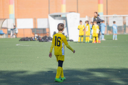 Rear view of Kid football player alone looking bench and coach on a competition matchの写真素材