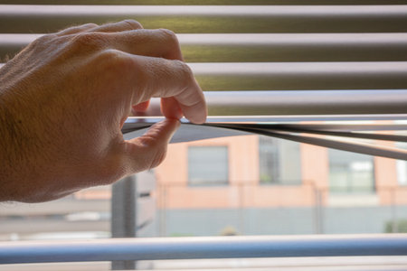 Mans hand revealing white venetian blinds. Looking out hiddenの写真素材