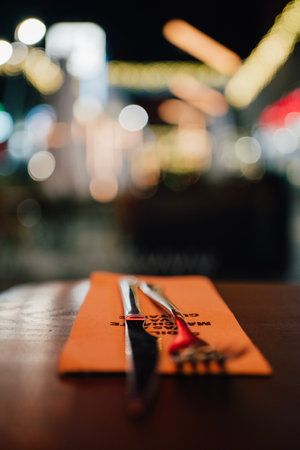 close up table setting in restaurant. Fork and a Knife and napkin.City night lights in backgroundの写真素材
