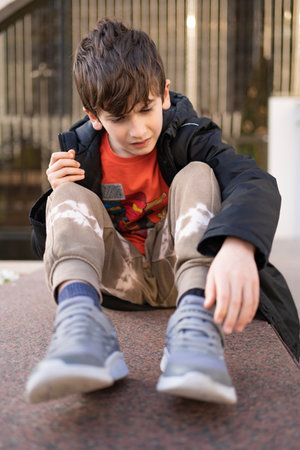 Worried young boy pain face hands joint hold leg pain because of ankle broken at outdoor streetの写真素材