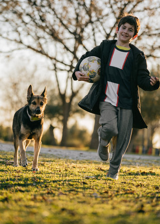 Kid with ball running from dog playing catch-up gameの写真素材