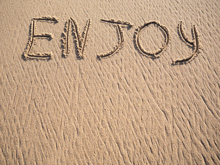 Enjoy word is written on the beach sand with copy spaceの写真素材