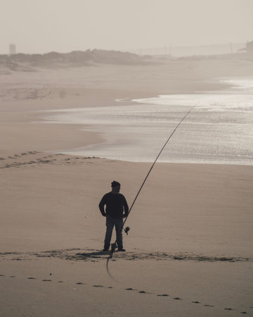 Silhouette of a fisherman with a rod on a beach alone