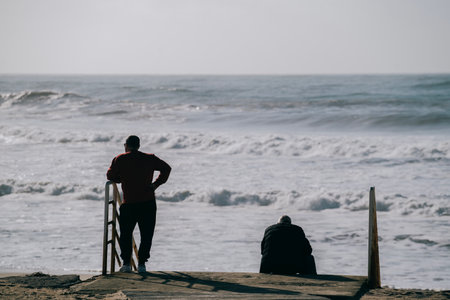 Silhouette of two adults looking at wild sea waves in calm and relaxed stateの写真素材