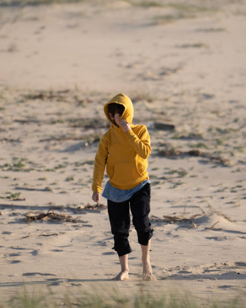 Kid enjoys hiding his face with hood in the beach sandの写真素材