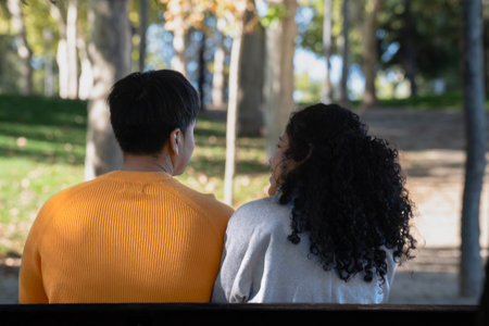 Rear view of young latin couple chatting on a bench in a parkの写真素材
