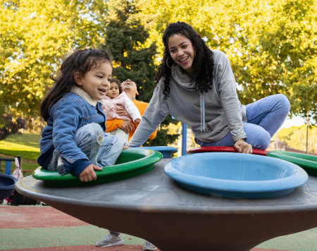Happy latin family laughing and enjoying together in a playground.Mom and son riding on a fun roundaboutの写真素材
