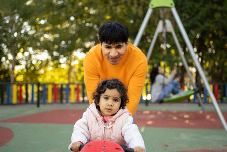 Young adult father pushing baby daughter on toy moto in playgroundの写真素材