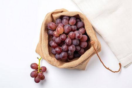 High angle view of red grapes on a rustic bag isolated on white backgroundの素材