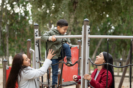 Kid having fun with his mother in a playground. Lesbian women mothers with their son playing in a jungle gym.の写真素材