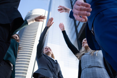 Young team of business executives raising arms while standing outdoors in an office area.の写真素材