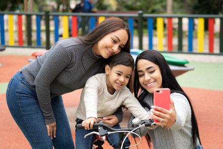 Happy smiling lesbian mothers taking a selfie with their son in a playground.の写真素材