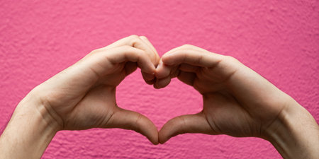 Hands forming a heart shape isolated on pink background.の写真素材