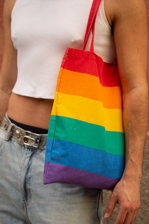 A man is holding a rainbow tote bag.The man is wearing a white shirt and blue jeans. Concept of pride and inclusivity.の写真素材