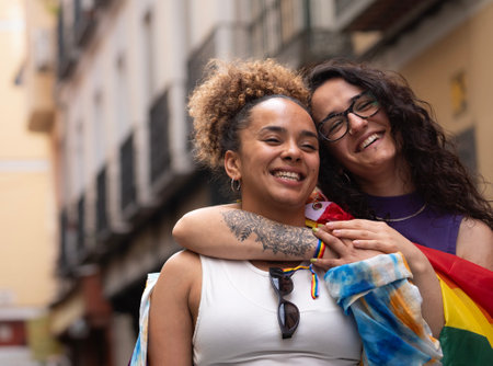 Two multiethnic happy lesbian women are hugging and smiling enjoying time in Madrid city street.の写真素材