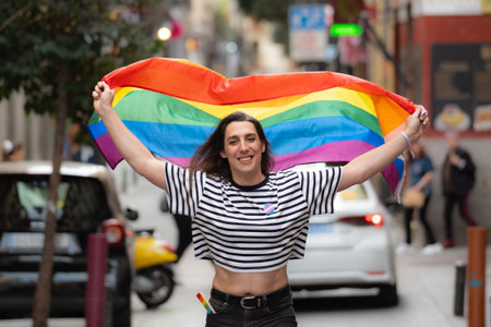Portrait of a happy transgender girl waving a rainbow flag in a city street. LGBTQ community and diversity concept.の写真素材