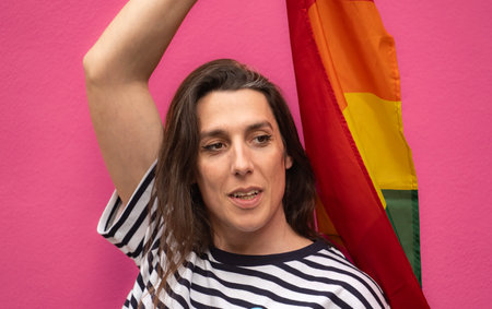 Headshot of a happy transgender woman holding a rainbow flag isolated on pin background.の写真素材