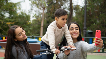Lesbian mothers taking a funny selfie with her son outdoors in a park. Diversity and LGBT family...