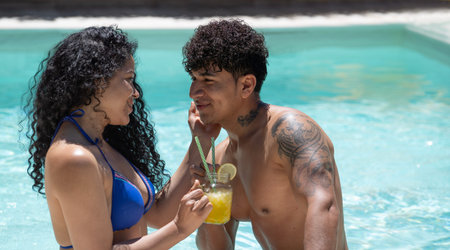 Young dominican couple are flirting on their first date in a turquoise water pool drinking a...