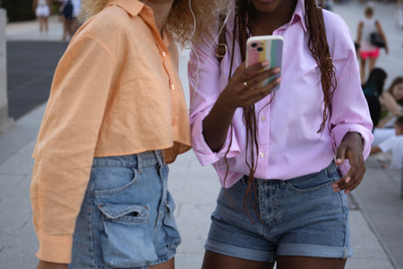 Two unrecognizable multiethnic young women are standing together and looking at a smartphone.