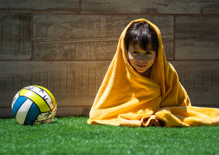 Young latin boy is drying in a yellow towel in summer vacations next to his ball.の写真素材