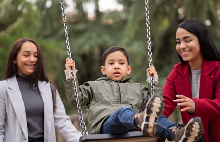 Portrait of hispanic lesbian couple having fun with their son on a swingの写真素材