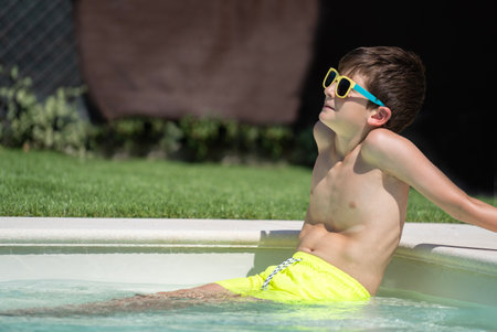 Side view of a child boy relaxing sitting in a pool and sunbathing with copy space.の写真素材