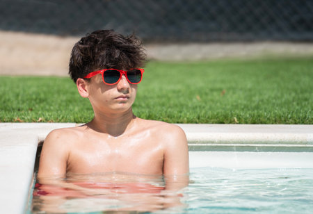 Front view of handsome teenager boy relaxing in a pool on a summer day with copy space.の写真素材