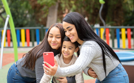 Hispanic lesbian family taking a selfie on a playground as a good time memory together.の写真素材