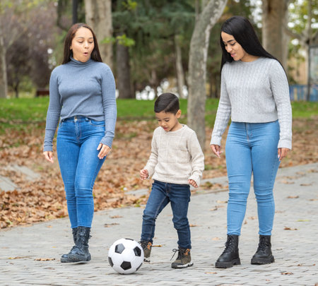 Young boy is playing soccer in the park with two young women cheering him onの写真素材