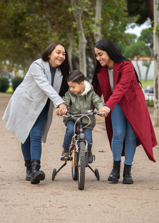 Two smiling women teaching their son to ride a bike on a path in a parkの写真素材