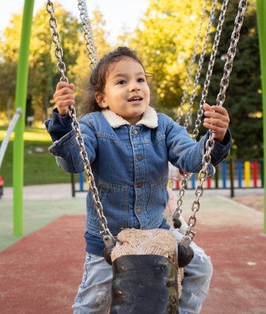 Front view of a happy dominican kid boy having fun in a swing outdoors.の写真素材
