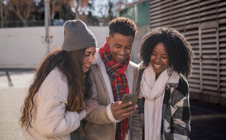 Group of cheerful multi-ethnic students looking at mobile phone and smiling, enjoying winter day...