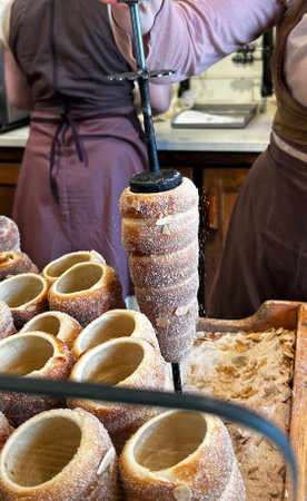 Pastry chef baking a kurtos kalacs, a traditional hungarian sweet pastry, sprinkling it with sugar and chopped almondsの写真素材